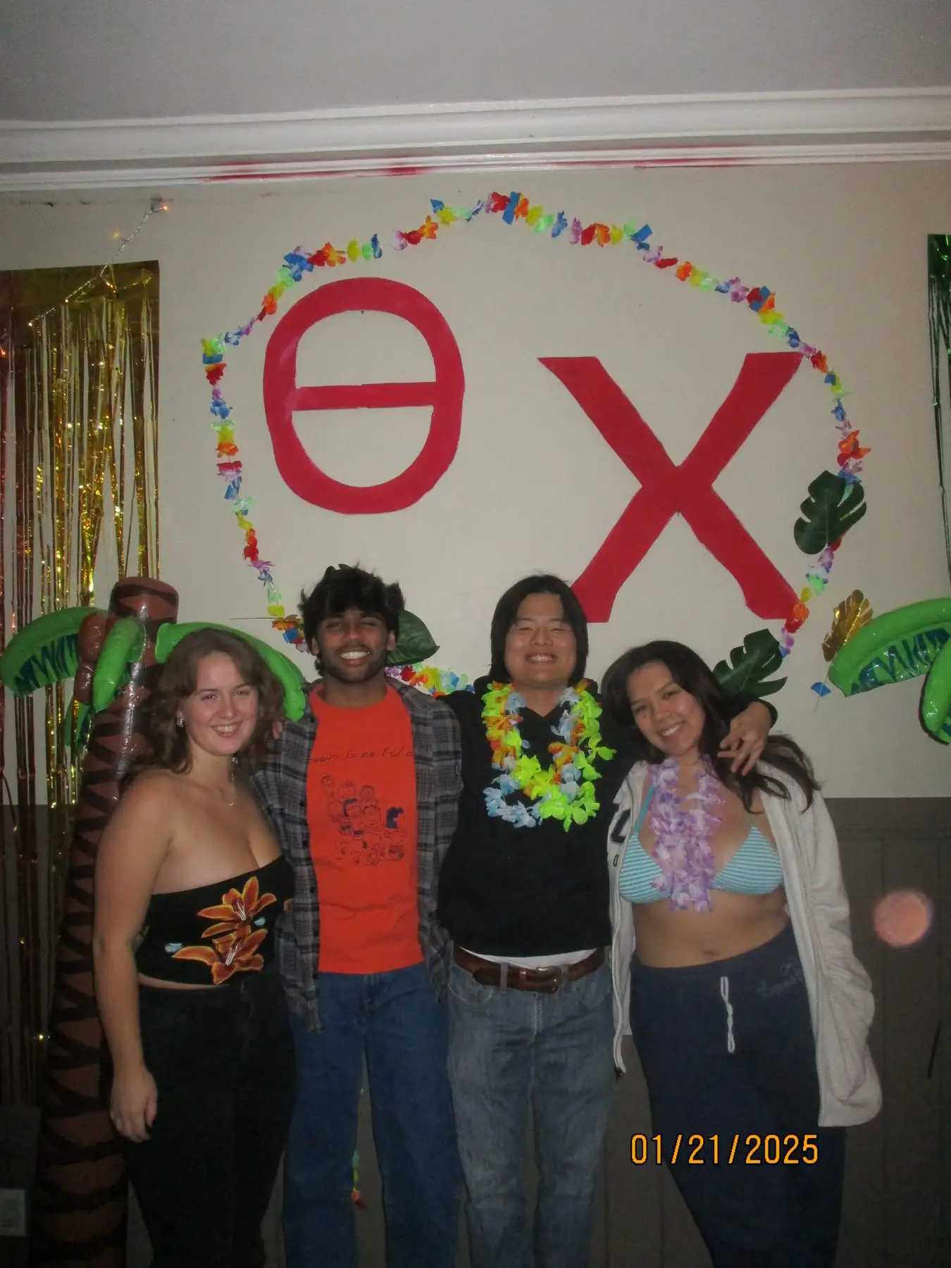 Friends in leis under painted Theta Chi letters at the luau night