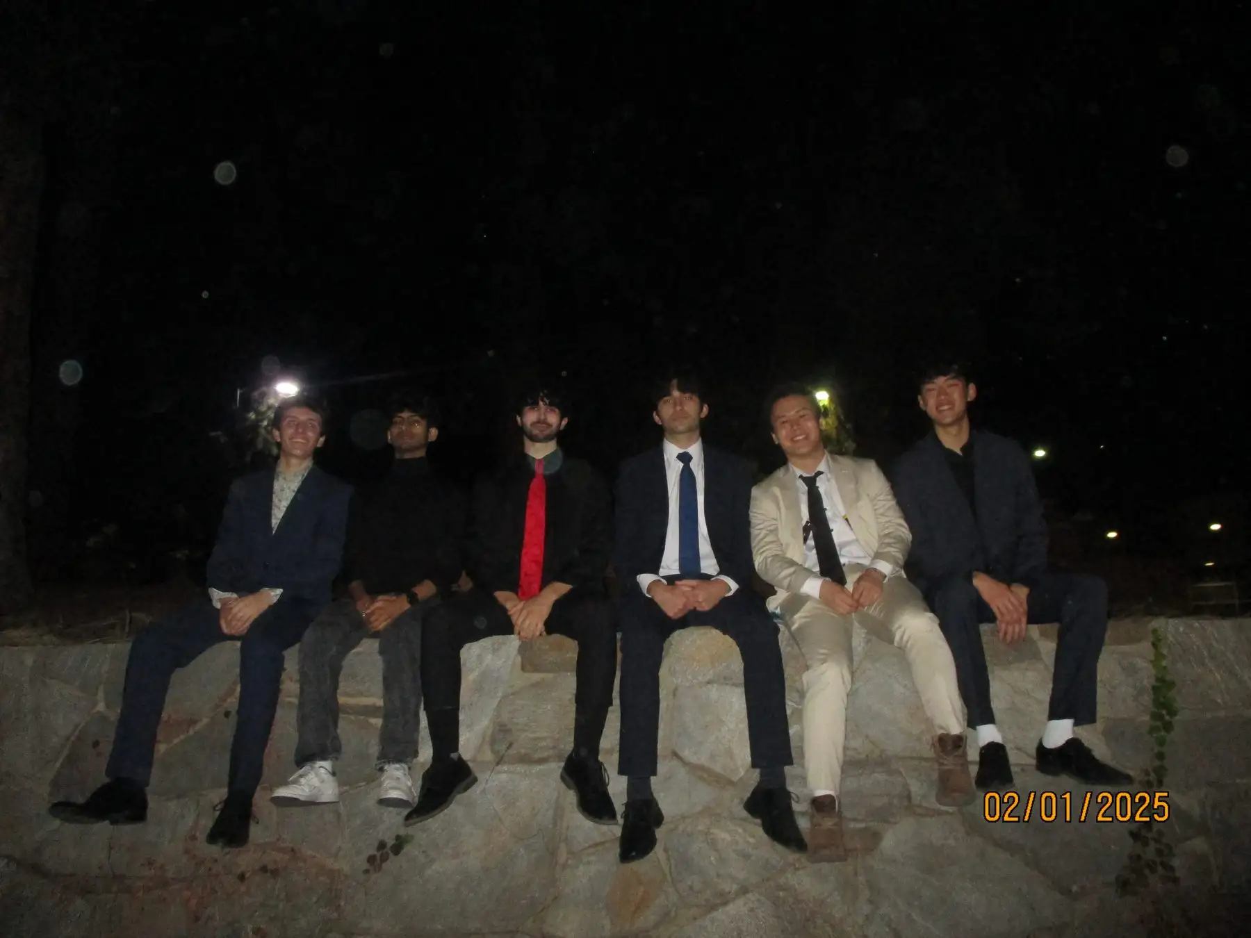 Six brothers in suits seated on a stone wall before formal