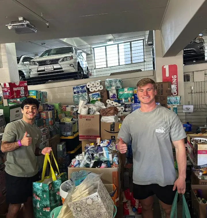 Two brothers giving a thumbs up among boxes of donated supplies at a YMCA donation drive