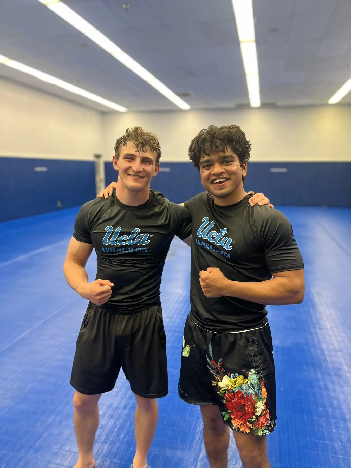 Two brothers in UCLA Brazilian Jiu-Jitsu gear flexing on the mats