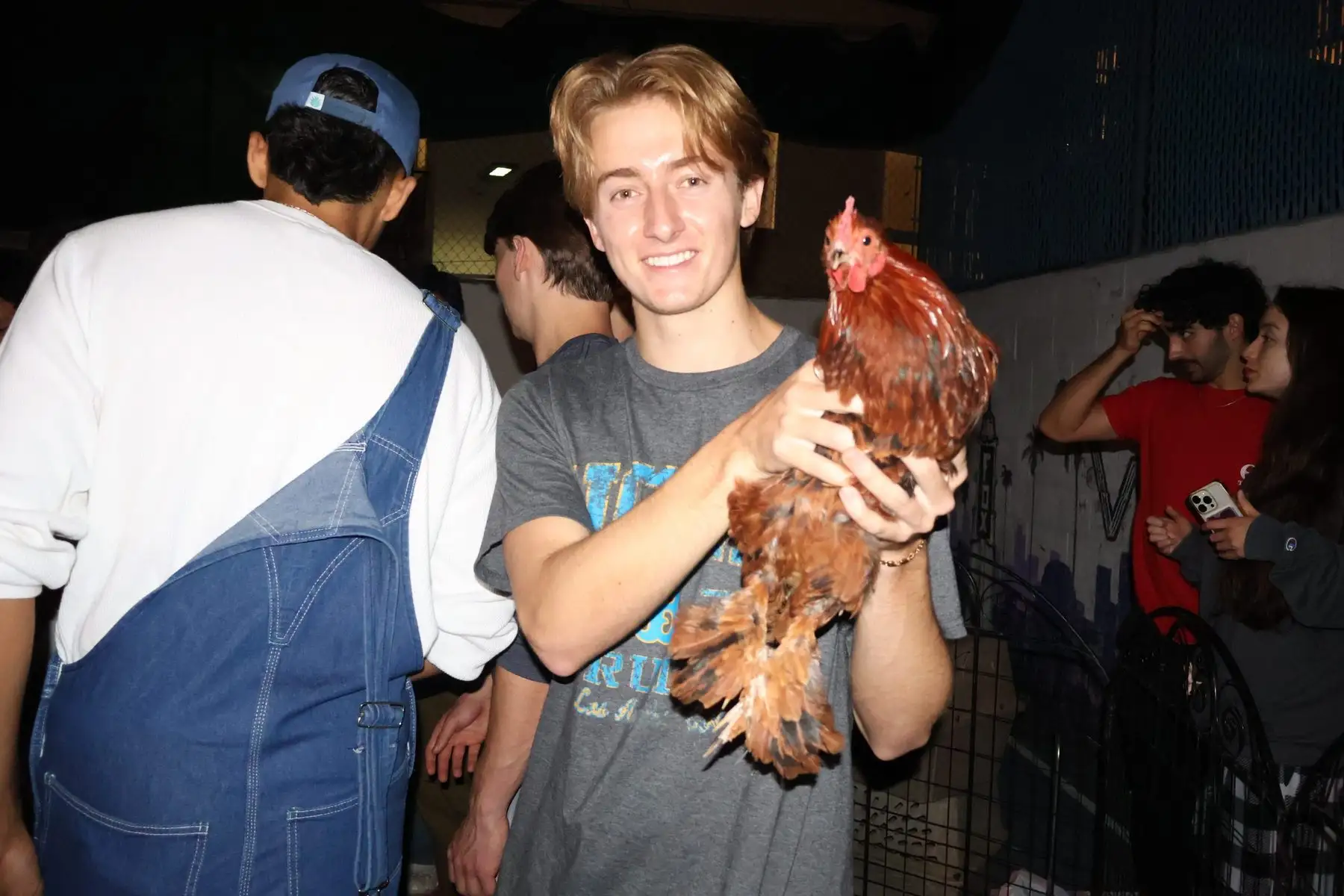 A smiling brother in a UCLA shirt holding a chicken at the petting zoo event