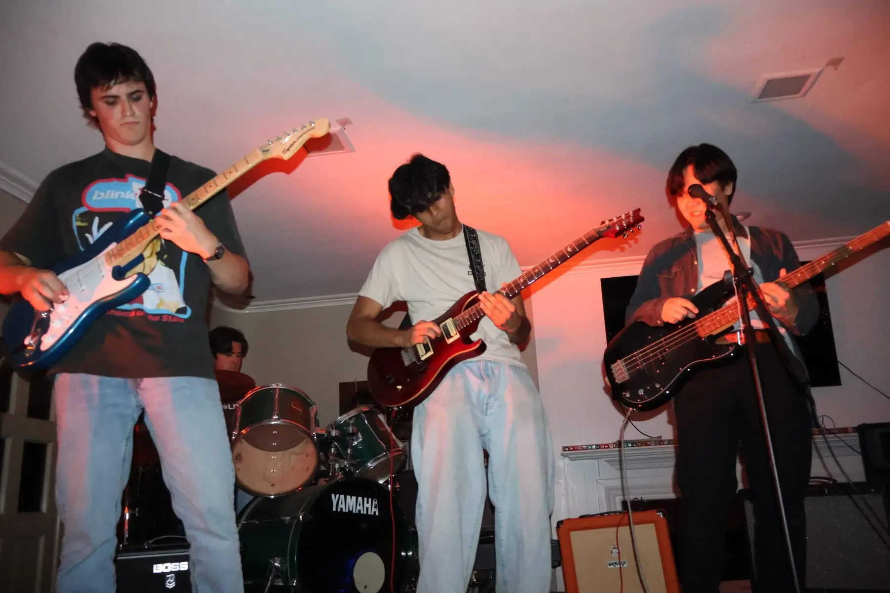 The house band playing guitars and bass under warm red light at a backyard show
